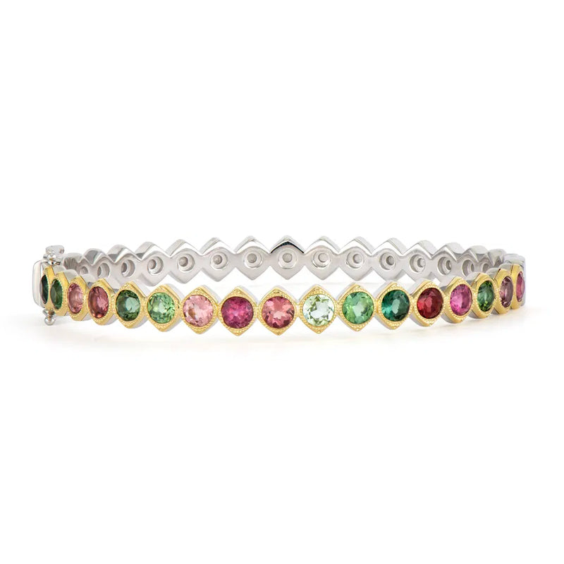 The Wish on a Star Two-Toned Bezel Tourmaline Bangle by Three Stories Jewelry is adorned with vibrant pink and green tourmaline gemstones, bordered by small 14K yellow gold settings. It features a sterling silver band with a zigzag design, and the clasp is visible on the left end.