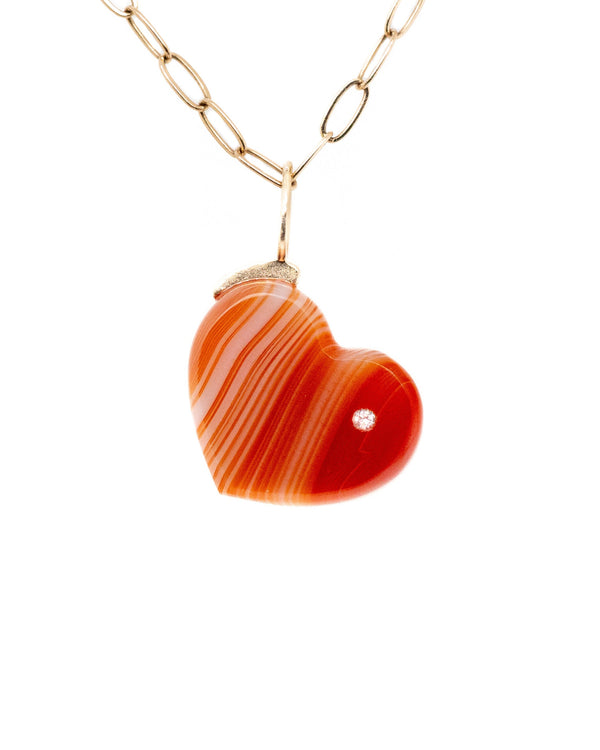 The Carnelian Heart necklace by Karen Luvaas features a gold chain and an orange, striped heart-shaped pendant with a small gem, shown against a white background.