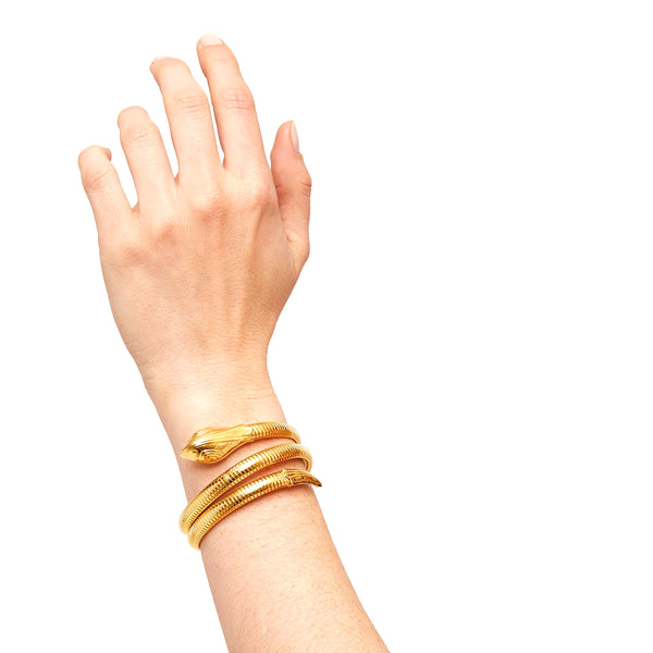 A hand showcases the gas bijoux Serpent bracelet—a gold plated, coiled snake design with visible head and tail—set against a plain white background.