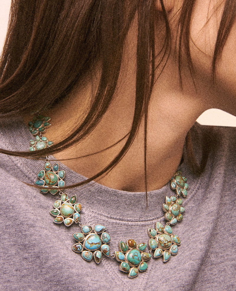 A person in a gray sweatshirt wears the Pascale Monvoisin Necklace GLORIA N°2, featuring exquisite turquoise stones in floral patterns. The elegant Silver 925 piece rests on their collarbone, complementing their long brown hair.