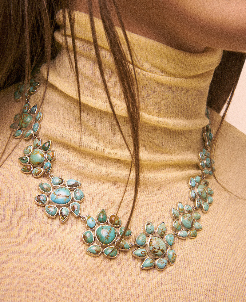 A woman in a beige turtleneck showcases the Necklace GLORIA N°2 by Pascale Monvoisin, featuring clusters of turquoise gemstones in floral patterns with shimmering Silver 925 elements for a bold, artistic accessory.