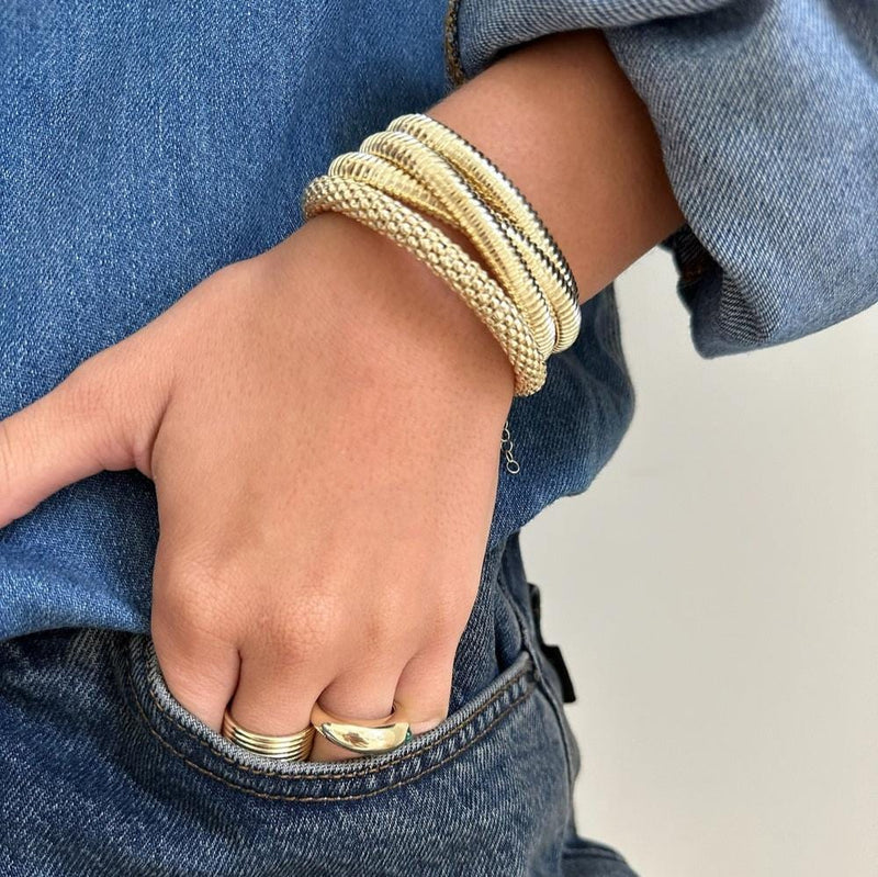 Close-up of a person's hand tucked into a jeans pocket, exuding timeless elegance with several gold vermeil bracelets, including the Aisha Bracelet by Jennifer Zeuner, alongside two gold rings on the middle finger. The person is stylishly dressed in denim.