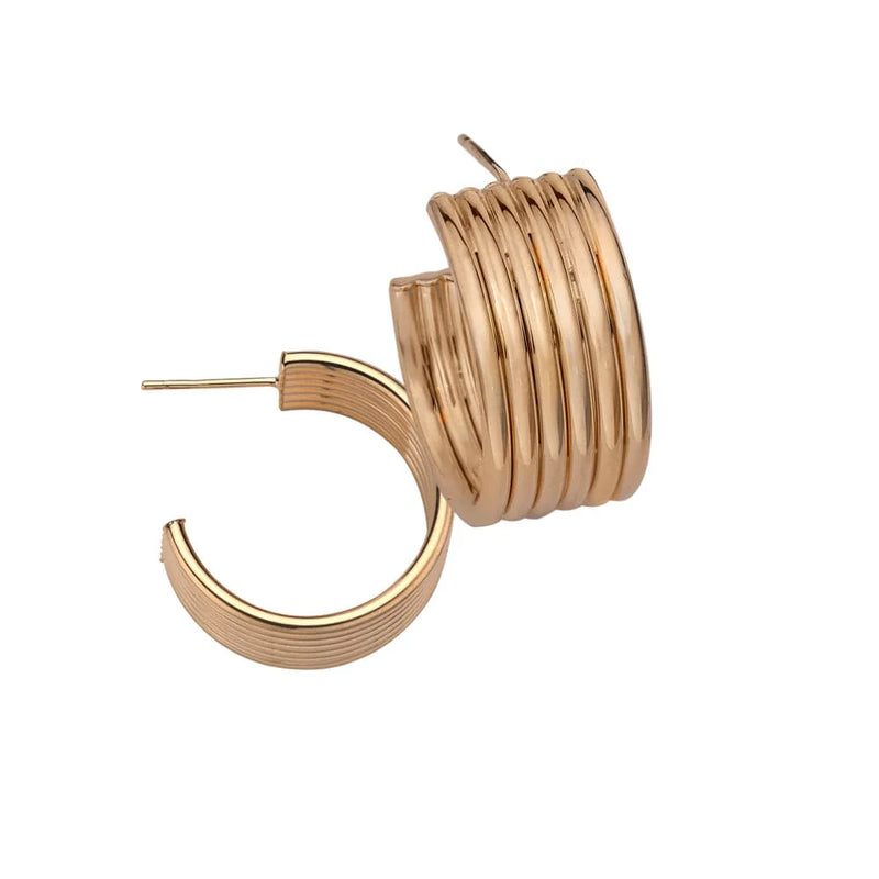 The Jennifer Zeuner Cairo 1 Hoops are crafted from 18k yellow gold-toned metal with a ridged texture, featuring trend-setting curved designs. One earring stands upright and the other lays beside it, highlighting their shiny surface.