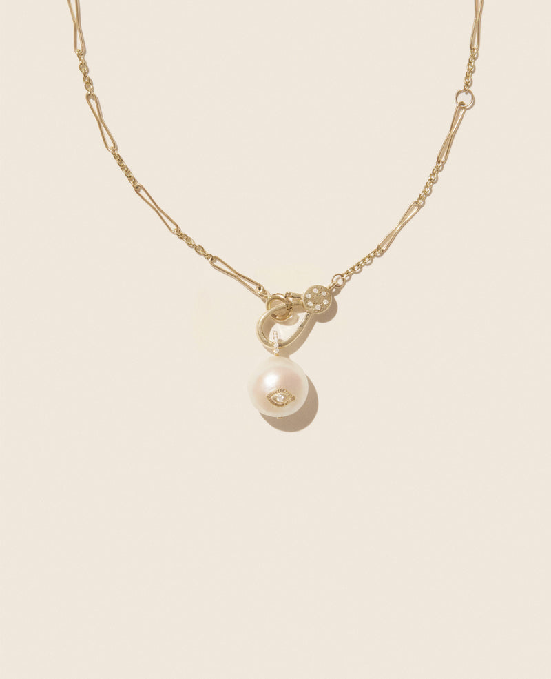 The Marcia Necklace by Pascale Monvoisin features a delicate yellow gold chain with a pearl pendant and flower charm. The adjustable chain combines different link styles for an elegant look, all set against a soft beige background.