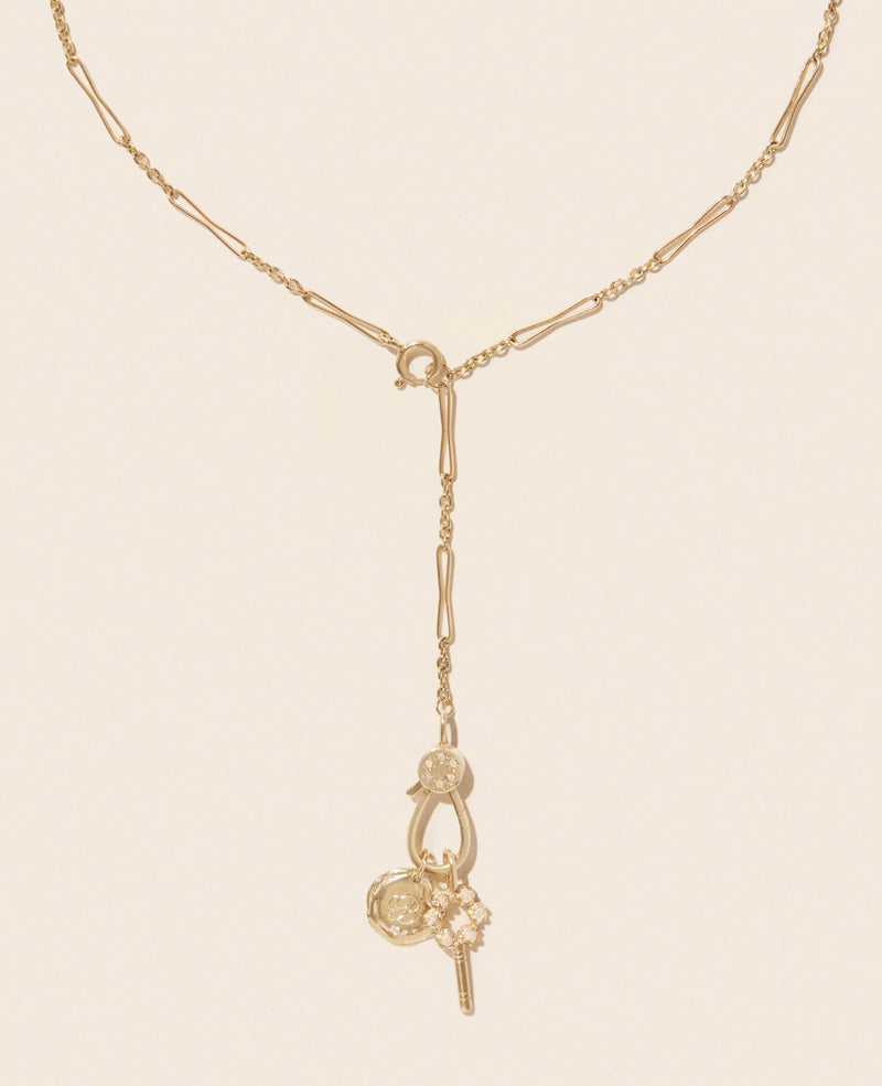 The Marcia Necklace by Pascale Monvoisin is a stunning yellow gold piece with an adjustable chain, featuring a Y-shaped pendant embellished with key and floral charms for an elegant, ornate look.