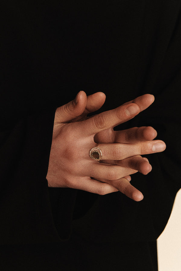 A person wearing a dark long-sleeved garment gently clasps their hands, showcasing a Pascale Monvoisin Rio Ring made of Silver 925‰ with an intricate design. The image highlights the ring and hands against a neutral background.