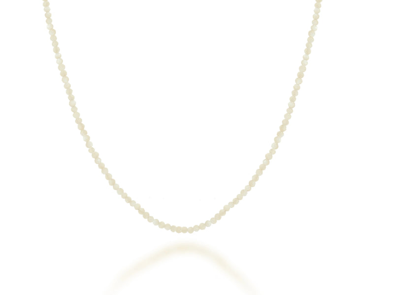 A single strand of small, round, white pearls forms the 28 Gemstone Bead Necklace by Rachel Reid, gracefully arranged in a gentle curve against a white background.