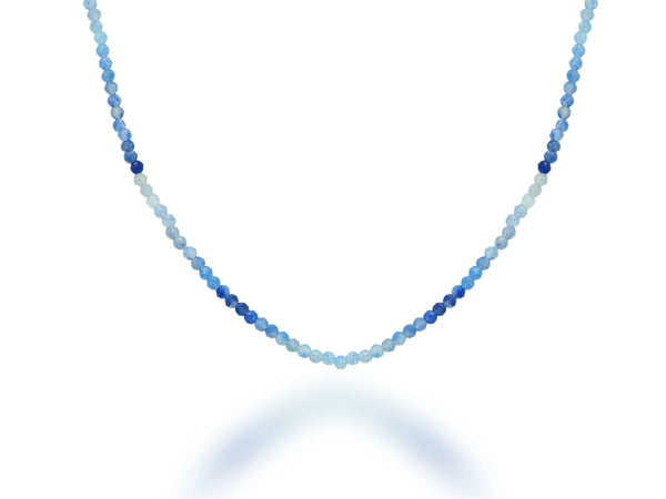 The Rachel Reid 28 Gemstone Bead Necklace features small, round beads in graduated blue shades, arranged from light to dark, with a lobster claw closure and shown on a white background.