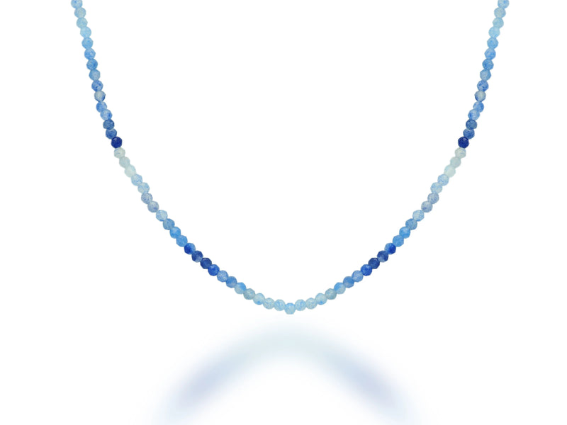 The Rachel Reid 28 Gemstone Bead Necklace features small, round beads in graduated blue shades, arranged from light to dark, with a lobster claw closure and shown on a white background.