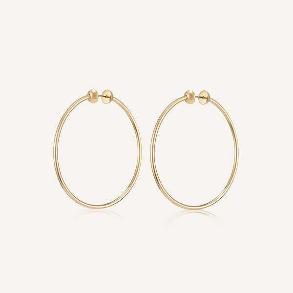 Introducing the Icon Hoops Medium by Jenny Bird: a pair of high-polish gold earrings made from stainless steel with small spherical studs at the top, perfect for adding elegance and simplicity against a plain, light background.