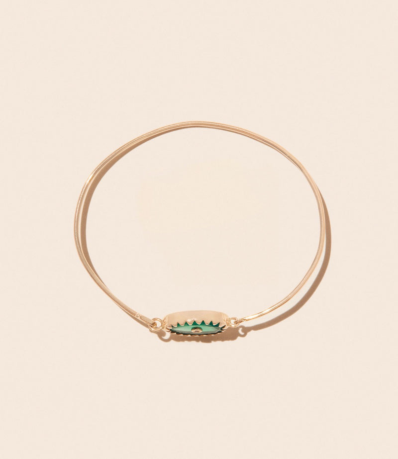 The Orso Bangle Green Onyx by Pascale Monvoisin is a simple gold bracelet featuring a thin band with an oval charm in the center. The charm boasts a green enamel zigzag pattern on a beige background, capturing the luxe bohemian essence of the brands designs.