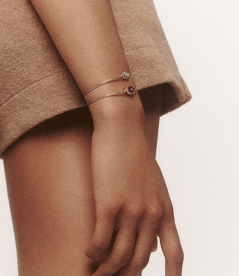 A persons arm showcases two Pascale Monvoisin bracelets, one with a unique stone. The Orso Bangle in Green Onyx adds charm, while the light brown garment complements the ensemble against a neutral background, ensuring these accessories remain the focal point.